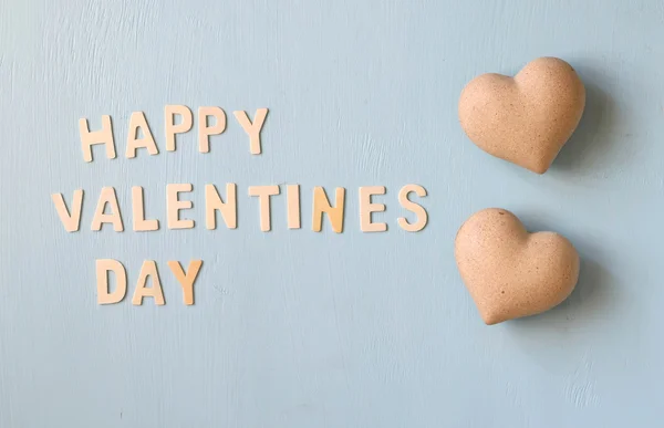 As palavras "dia feliz dos namorados" feitas com letras de madeira de bloco ao lado do par de corações no fundo de madeira azul claro . — Fotografia de Stock