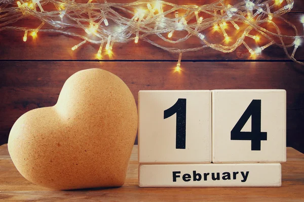 February 14th wooden vintage calendar next to heart on wooden table. vintage filtered — Stockfoto