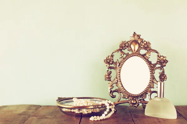 Antique blank victorian style frame, perfume bottle and white pearls on wooden table. retro filtered and toned. template, ready to put photography — Stockfoto