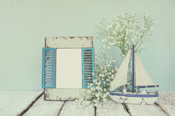 Old vintage wooden frame, white flowers and sailing boat on wooden table. vintage filtered and toned image. nautical lifestyle concept. template, ready to put photography — Stockfoto