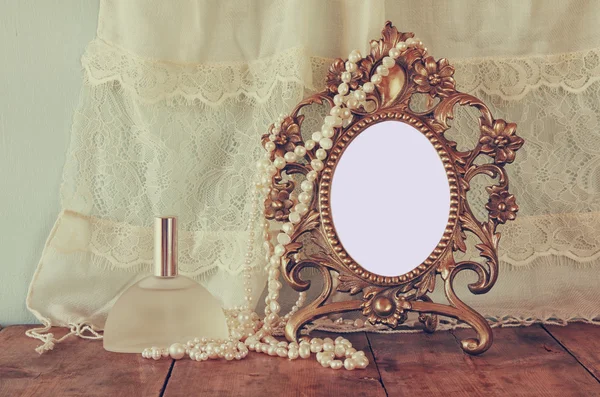 Antique blank victorian style frame, perfume bottle and white pearls on wooden table. retro filtered and toned. template, ready to put photography — Stok fotoğraf