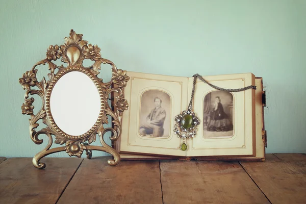 Antique blank victorian style frame and old open photograph album on wooden table. retro filtered image. template, ready to put photography