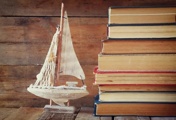 Stapel alter Bücher neben dekorativem Segelboot-Holztisch. Vintage gefiltertes Bild — Stockfoto