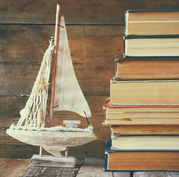 Pilha de livros antigos ao lado de mesa de madeira decorativa barco à vela. imagem filtrada vintage — Fotografia de Stock