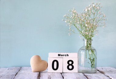 wooden March 8 calendar, next to heart and white flowers on old rustic table. selective focus