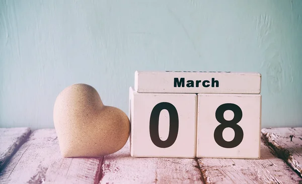 Vintage filtered image of wooden March 8 calendar, next to white heart on old rustic table. selective focus — Stock Photo, Image