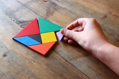 kayıp bir parça kare bir tangram tutan adamın el Bulmaca, ahşap masa üzerinde.