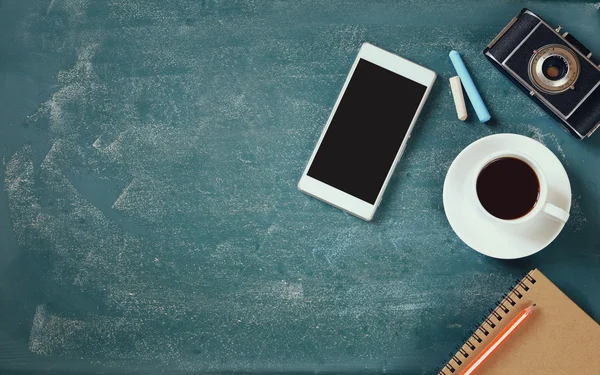 Top view image of mobile phone, cup of coffee, notebook and vintage camera over blackboard background — Stok fotoğraf