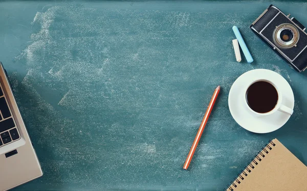 Top view image of cup of coffee, notebook, vintage camera and laptop over blackboard  background — Zdjęcie stockowe