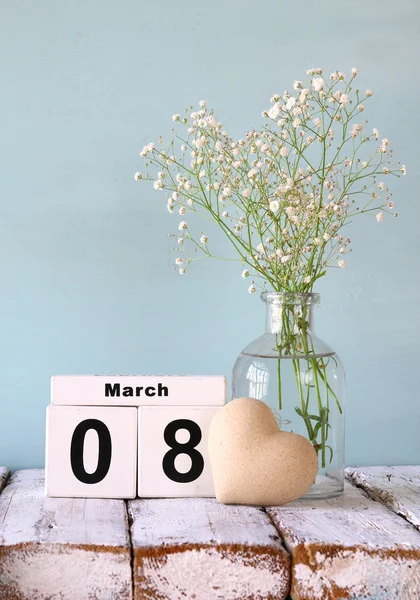 Wooden March 8 calendar, next to heart and white flowers on old rustic table. selective focus — ストック写真