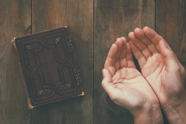 Top view image of mans hands folded in prayer next to prayer book. concept for religion, spirituality and faith — Stock Photo, Image