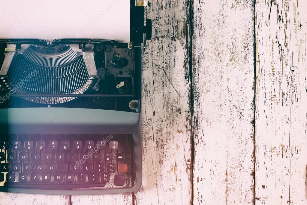 abstract vintage filtered image of top view photo of vintage typewriter with blank page, on wooden table