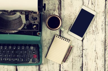 retro filtered image of vintage typewriter, blank notebook, cup of coffee and smartphone on wooden table