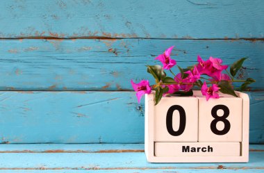 Tahta 8 Mart takvimi, eski mavi kırsal masadaki mor çiçeklerin yanında. Seçici odaklanma. Klasik filtrelenmiş