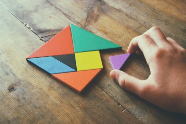 kayıp bir parça kare bir tangram tutan adamın el Bulmaca, ahşap masa üzerinde.