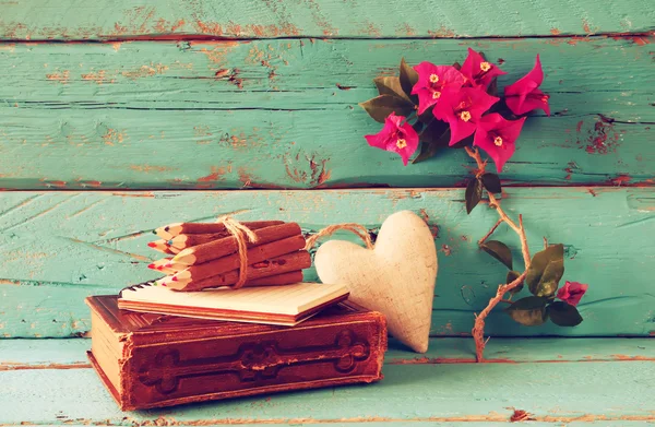 Vintage notebook and stack of wooden colorful pencils on wooden texture table next to purple bougainvillea flower. vintage filtered and toned image — Stockfoto