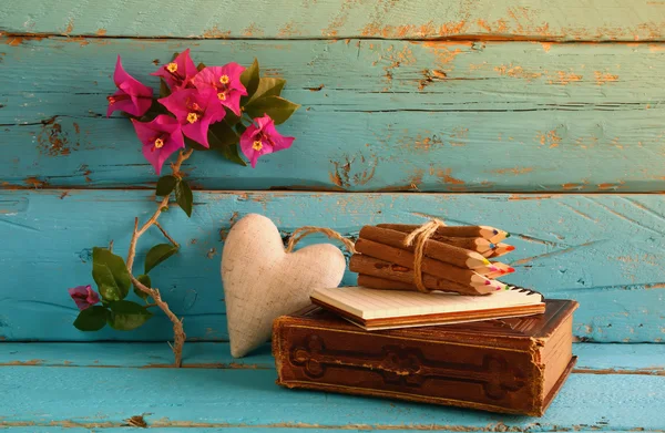 Vintage notebook and stack of wooden colorful pencils on wooden texture table next to purple bougainvillea flower. vintage filtered and toned image — Stockfoto