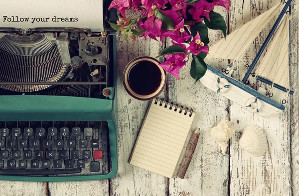 Bild einer alten Schreibmaschine mit dem Satz "Folgen Sie Ihren Träumen", leeres Notizbuch, eine Tasse Kaffee und ein altes Segelboot auf einem Holztisch — Stockfoto