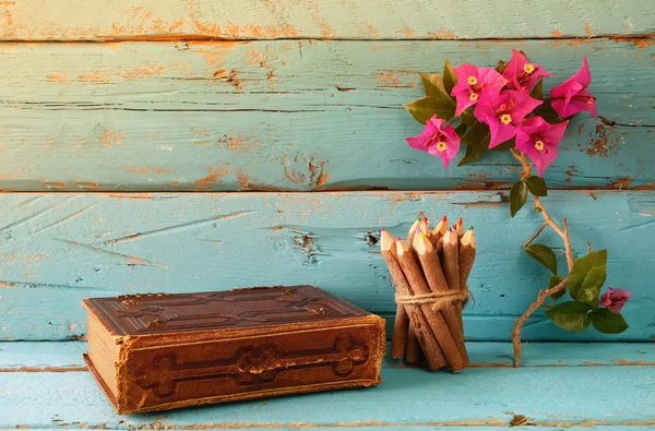 Vintage notebook and stack of wooden colorful pencils on wooden texture table next to purple bougainvillea flower. vintage filtered and toned image — Zdjęcie stockowe