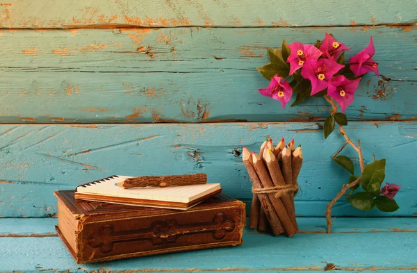 Caderno vintage e pilha de lápis coloridos de madeira na mesa de textura de madeira ao lado da flor de buganvília roxa. imagem filtrada e tonificada vintage — Fotografia de Stock