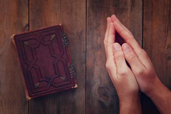 Top view image of mans hands folded in prayer next to prayer book. concept for religion, spirituality and faith. vintage filtered and toned — Stock Photo, Image