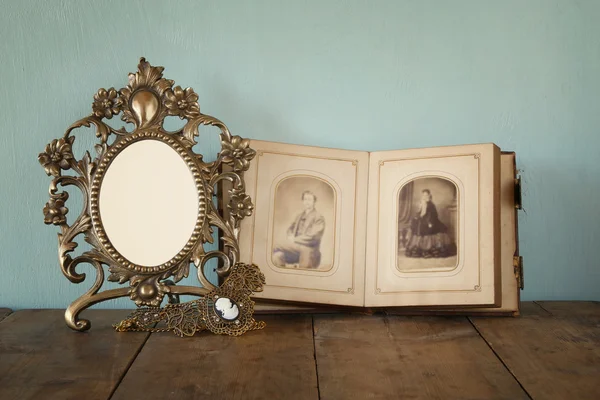 Antique blank victorian style frame and old open photograph album with vintage necklace on wooden table. retro filtered image. template, ready to put photography