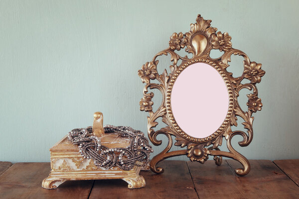 Antique blank victorian style frame and neckless on wooden table. retro filtered image. template, ready to put photography