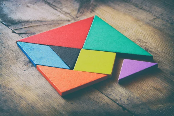 En saknad bit i en fyrkantig tangram pussel, över träbord. bleknat stil Foto — Stockfoto