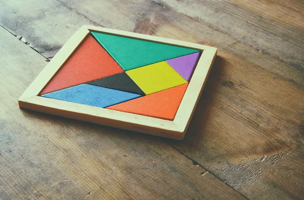 Uma peça perdida em um quebra-cabeça de tangram quadrado, sobre mesa de madeira. foto de estilo desbotada — Fotografia de Stock