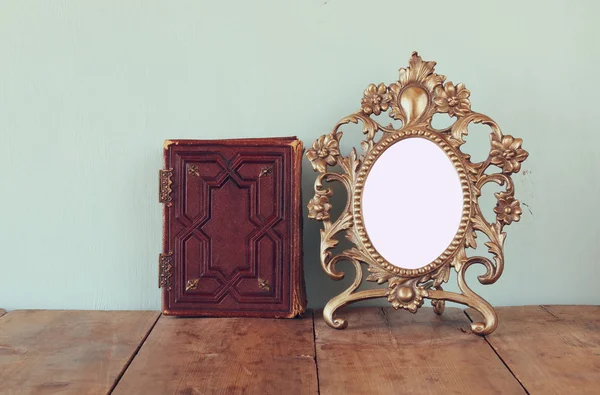 Antique blank victorian style frame and old book on wooden table. retro filtered image. template, ready to put photography — Stockfoto