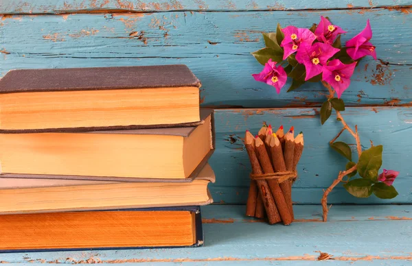 Pila de libros antiguos junto a coloridos lápices y flores de buganvillas en la mesa de madera. vintage imagen filtrada — Foto de Stock