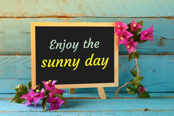 Blackboard over blue wooden shelf with the phrase ENJOY THE SUNNY DAY. — Stock Photo, Image
