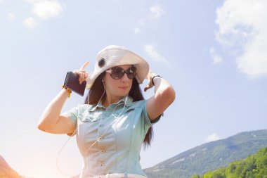 Moda kız büyük beyaz bir şapka ve güneş gözlüğü bir smartphone cep telefonu ile müzik dinlemek.