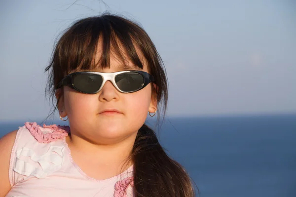 Meisje in zonnebril op zonsondergang kijken naar de camera, tegen een achtergrond van de zee — Stockfoto