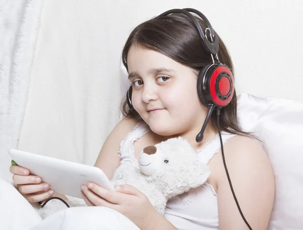 Lány ül a fehér ágyban zenét hallgatni, kezében tabletta — Stock Fotó