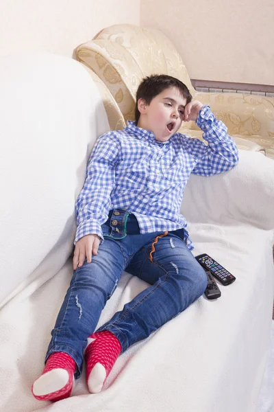 Мальчик лежит на диване с пультом и зевает. — стоковое фото