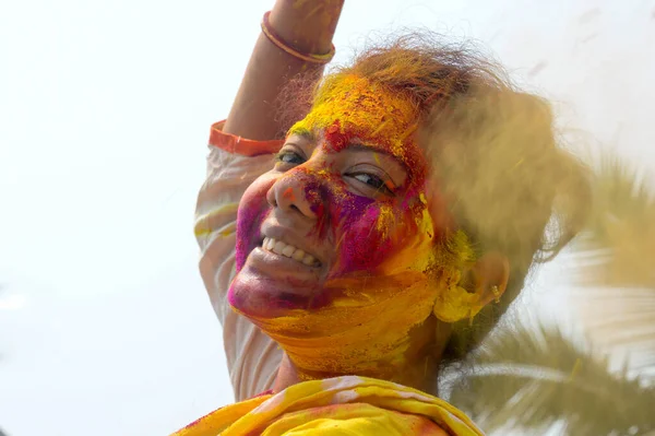 Portrait Of One Young Indian Happy woman with pink, yellow and red Holi colored powder paint on face During Holi Color festival. Front View. Looking at camera.