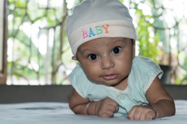 Sevimli bebek başını kaldırıyor. Yakından bir portre. Mutlu çocuk kameraya bakıyor ve gülümsüyor. Sağlık hizmetleri tıbbi geçmişi. Tatlı, küçük bir bebek. Hint etnik kökeni. Bebek için gelişimsel kilometre taşı.