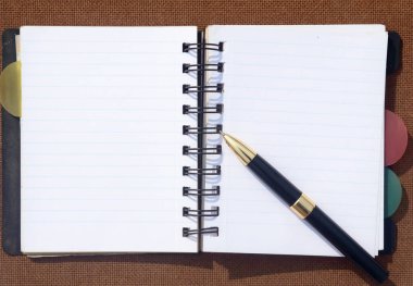 Kahverengi renkli sert mantar tahtasının üzerine açık bir defter yerleştirilmiş bir kalem. İş Eğitimi geçmişi.