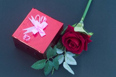 Kırmızı bir gül ve mavi arka planda kurdeleli bir hediye kutusu. Yüksek açı. Düz Yat. Metin için boşluk kopyala.