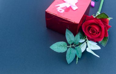 Kırmızı bir gül ve mavi arka planda kurdeleli bir hediye kutusu. Yüksek açı. Düz Yat. Metin için boşluk kopyala.
