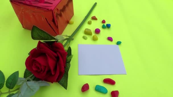 礼品盒上系着彩带和红玫瑰的蝴蝶结 桌上放着一张浅绿色背景的空白贺卡 平躺在床上情人节 周年纪念日或节日庆祝装饰的设计 — 图库视频影像