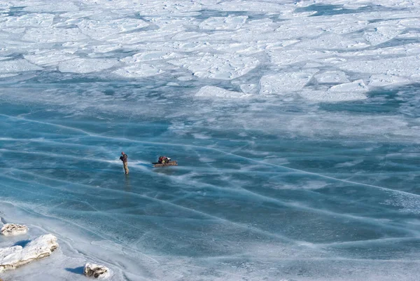 在湖上的冰上远足.一名男子在俄罗斯贝加尔湖冰上拖着一辆装有货物的雪橇 — 图库照片
