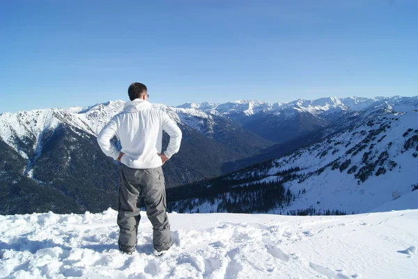 Um homem fica em frente a um panorama de montanhas, uma vista de trás — Fotografia de Stock