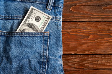 Para cepte. Ahşap bir arka planda kot pantolonun arka cebinde 100 Amerikan doları var. Uzayı kopyala Para kazanma ve biriktirme kavramı. Amerikan parası