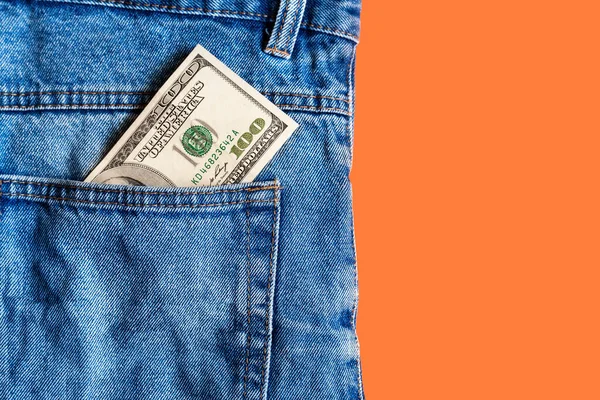 Money in pocket. One hundred dollar bill in a denim jeans pocket on a orange background. Copy space. Concept of earning and saving money. American money