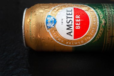 Su damlalı bira kutusu. Yoğunlaşmayla kaplı bir kutuda AMSTEL birası. Dünyaca ünlü Hollanda markası. Fotokopi alanı olan siyah ıslak arka plan. Seçici yumuşak odaklanma. Kiev. Ukrayna. Haziran-26.2021.