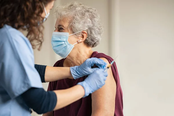 의사가 진료소에서 공간으로 환자에게 접종을 병원의 나이든 여성에게 주사를 주사기를 — 스톡 사진
