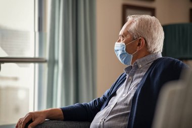 Korumacı maskeli yalnız bir son sınıf öğrencisi karantina sırasında evde oturuyor. Depresyonda olan yaşlı bir adam, Coronavirus 'a karşı güvenlik için yüz maskesi takarken koltukta dinleniyor. Düşünceli yaşlı yalnız başına Quara sırasında pencereden dışarı bakıyor.
