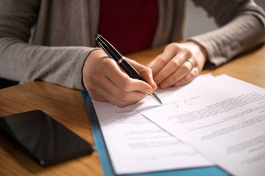 Close up of hands of young woman signing legal documents on desk. Close up of woman hand holding pen and signing legal paper seated at desk. Detail of lawyer filling official document, deal done. clipart